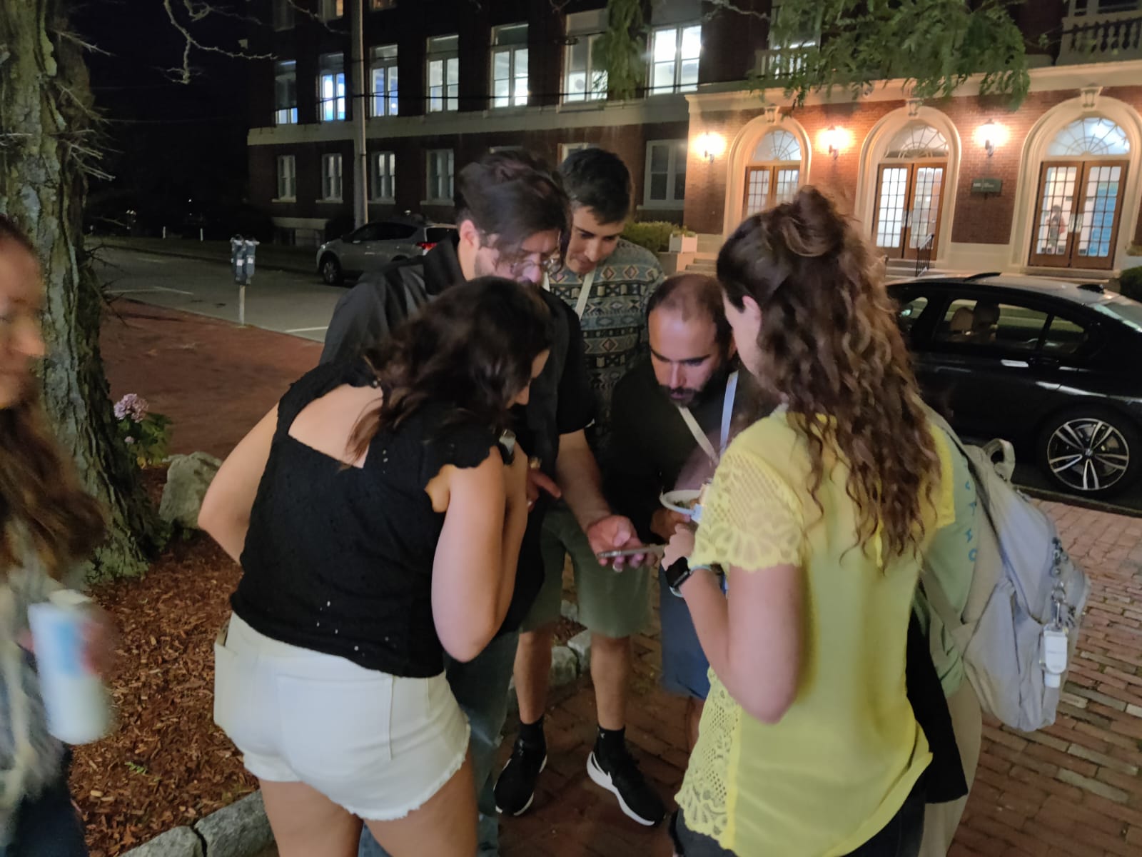 Five people stand in a circle looking at a phone.