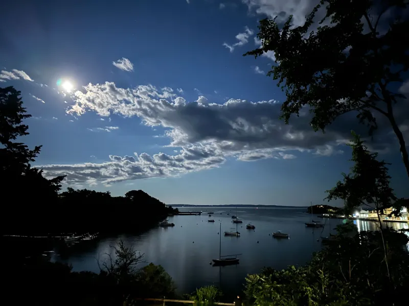 a lake with a bright moon and clouds above it.