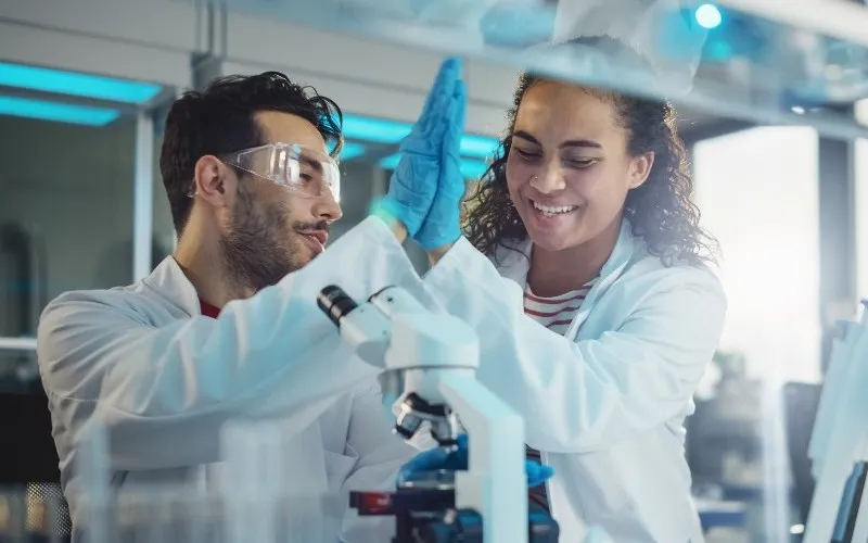Two scientists use a microscope at a lab station. 