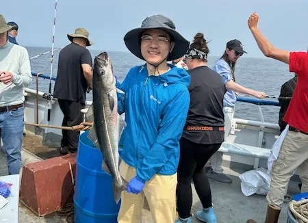 man in blue coat and sun hat on a boat holding a fish
