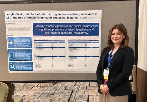 Woman with brown hair in business formal attire standing in front of a poster presentation