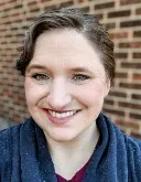 Headshot of Becca Hayes, a woman with her brown hair tied back smiles at the camera.