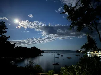 a lake with a bright moon and clouds above it.